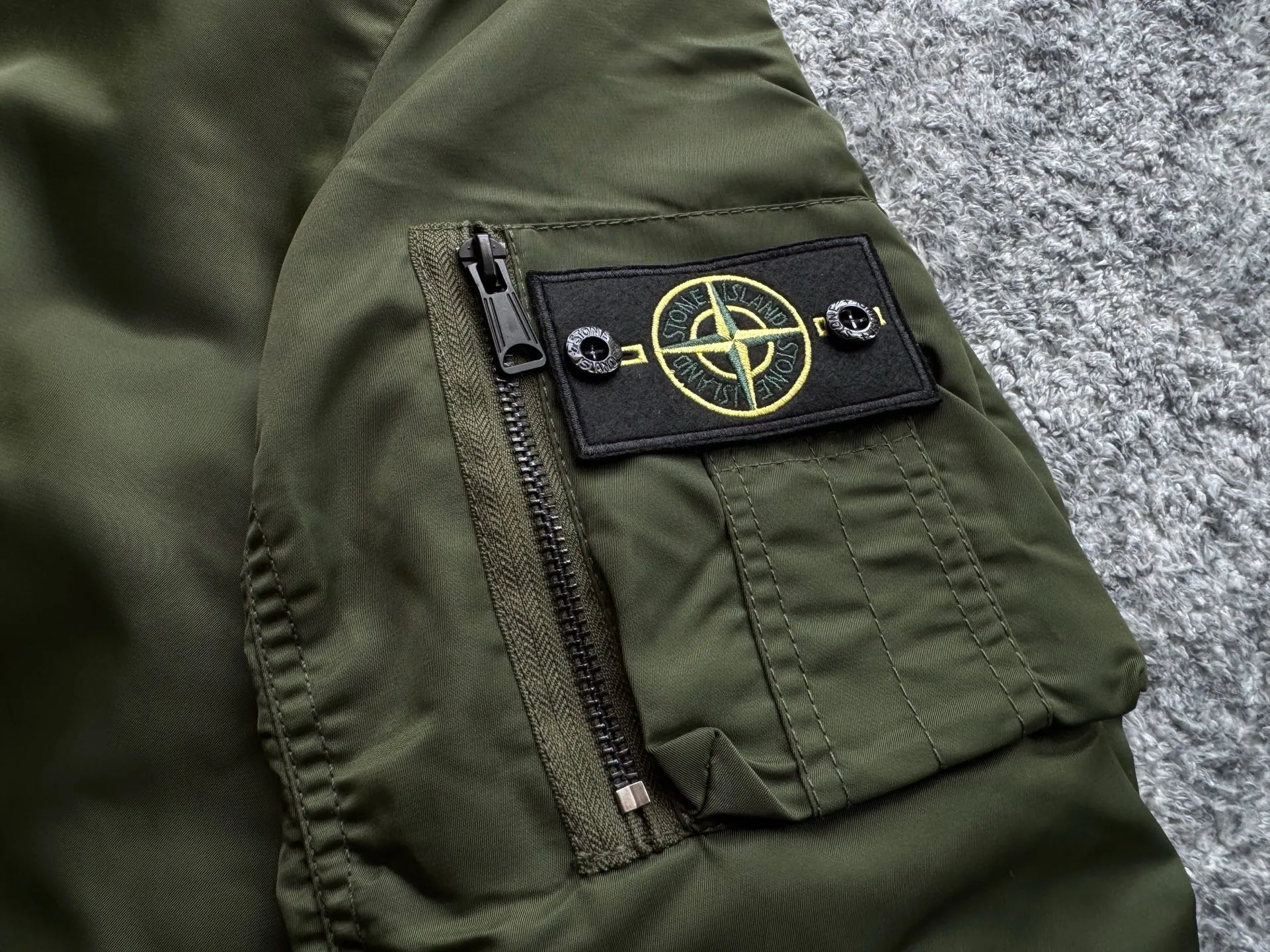 P360 Stone lsland Stone Island Medal Aviator Cotton Jacket The outer fabric is made of MA-1 flight nylon, which is a material specially used in flight and aviation. Flying nylon is a fabric specially used in flight and aviation. It is rarely used in ordinary clothing. The density of flying nylon is very high, so it is windproof and waterproof. When rain falls on the surface of the clothes, it will not penetrate immediately, but will form a small water droplet and slide off. This performance is a requirement for the development of modern jet technology. Because it is assumed that the pilot got caught in the rain before getting on the plane, he entered the cabin covered in rainwater. When flying at high altitude and at high speed, in a cabin without an environmental control system, water droplets will freeze on the pilot's body 2. Knitted baseball collar MA-1 uses a knitted collar. The collar is made of wool and can be snug around the neck and very warm. 3. Metal zippers We have very strict requirements on zippers, including smoothness and size. There was no zipper on the market that met the requirements, so we asked a zipper factory to customize a strong and durable metal zipper.  4. Double-threaded knitted cuffs The cuffs are made of double-threaded knitted fabric, narrow at the front and wide at the back. The narrow part can be tightened around the wrist to prevent wind from entering. The wide part has enough space when wearing multiple pieces under winter Color: Black Dark Army Green Size: M L.